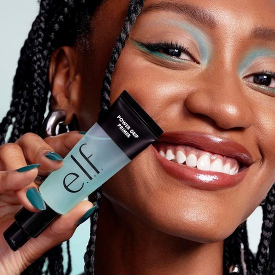 Model met donkere vlechten en turquoise oogschaduw houdt een transparante e.l.f. Power Grip Primer vast.