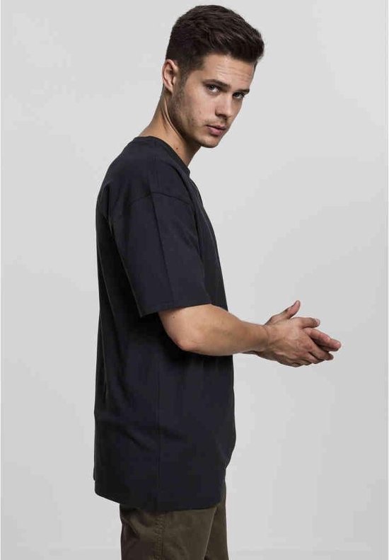 Man, zijaanzicht, draagt een donkergrijs oversized T-shirt met korte mouwen.