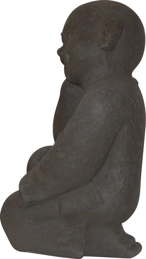 Vue de côté d'une statue de Bouddha enfant en pierre gris foncé, assise en tailleur, tête sur la main.