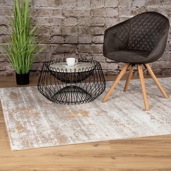 Beige-bruin vloerkleed in een woonkamer met een zwarte stoel, een metalen bijzettafel en een plant.