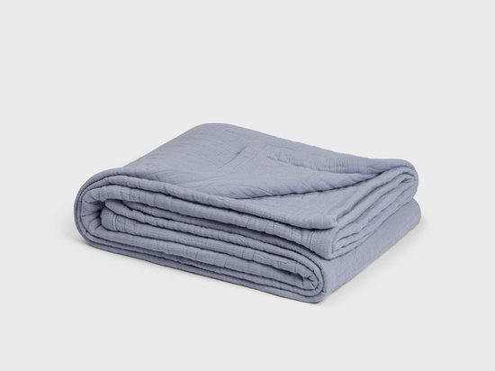 Opgevouwen lavendelblauwe mousseline spreideken met lijnenpatroon.