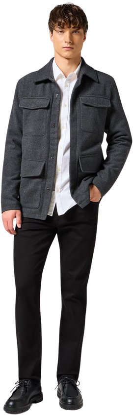 Model in een grijze jas met vier zakken, wit overhemd en zwarte jeans.