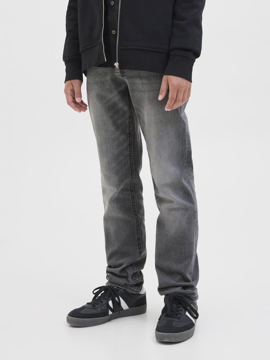 Close-up van de benen van een jongen in grijze jeans en zwarte sneakers.