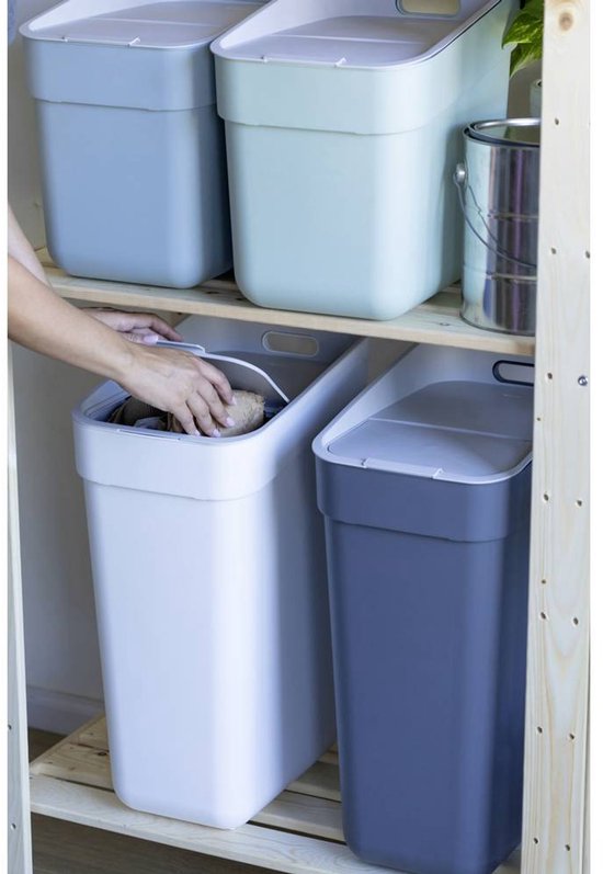 Deux poubelles grises et bleu clair avec couvercles, sur une étagère en bois. Une personne prend une poubelle blanche avec couvercle.