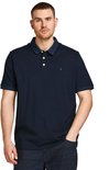 Man in donkerblauw poloshirt met navy kraag en knoopjes, met hand in broekzak.