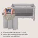 Grijs reisbedje met gaas, matras en een vrouw die de matras vasthoudt.