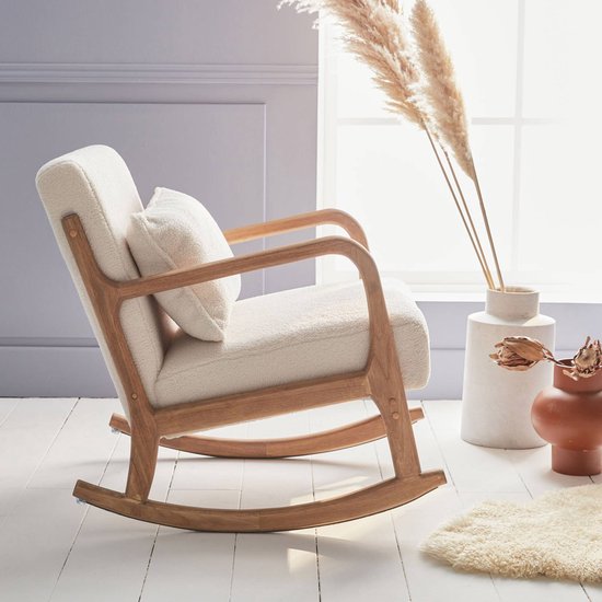 Schommelstoel met walnootkleurig houten frame en crème bouclé bekleding, geplaatst in een lichte kamer met pampasgras.