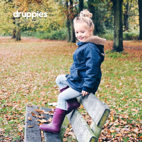 Meisje met blonde knot, spijkerjas en paarse laarzen, zittend op een houten bankje in een herfstbos.