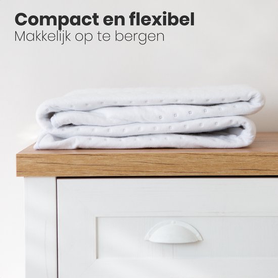 Een opgevouwen witte elektrische deken met een subtiel ruitpatroon op een houten lade.