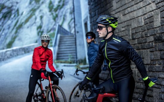Drie fietsers in racekleding, waarvan één op de voorgrond een zwart fietsjack met fluor details draagt.
