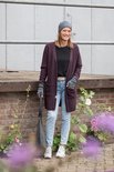 Vrouw met lang paars gebreid vest, grijze muts, vingerloze handschoenen en grijze tas.
