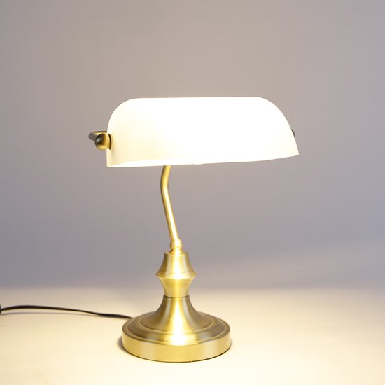 Lampe de bureau dorée avec abat-jour en verre blanc, posée sur une table.