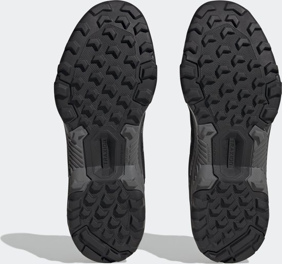 Onderkant van twee zwarte lage wandelschoenen met een grof profiel en het 'Traxion'-logo.