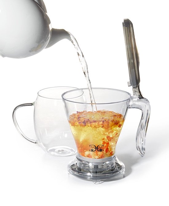 Transparante theepot met handvat en deksel, gevuld met bloemeninfusie, krijgt water uit een witte theepot gegoten.
