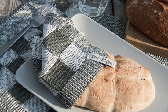 Wit brood op een grijs-wit geblokte placemat met een gevouwen vaatdoek met ruitpatroon.