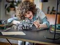 Een jongen met krullend haar speelt met een LEGO Spider Tank en minifiguren.