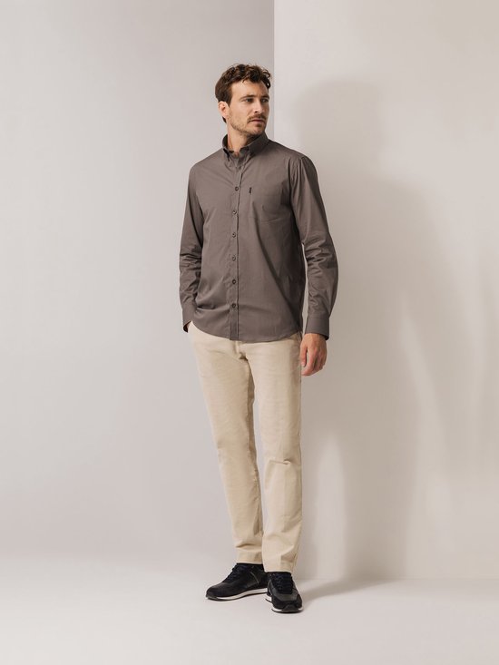 Man met beige broek en bruin hemd met print, handen in zakken.