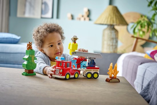 Un jeune enfant joue avec un camion de pompiers LEGO Duplo, un arbre, un écureuil et des flammes.