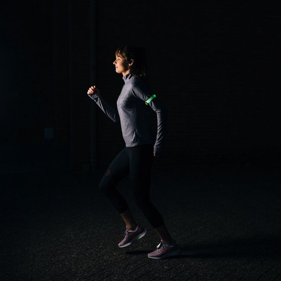 Vrouw met groene verlichte Bee-Safe armband tijdens het hardlopen in het donker.