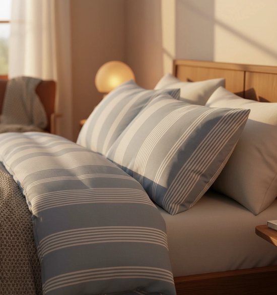 Close-up van kussens met blauwe en witte strepen op een bed met houten hoofdeinde, zacht ochtendlicht.