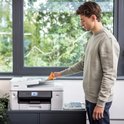 Man laadt oranje papier in een witte Brother printer, met groen tenue.