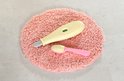 Een roze, ronde, zachte mat met een gele thermometer en een roze lepeltje.