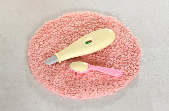 Een roze, ronde, zachte mat met een gele thermometer en een roze lepeltje.