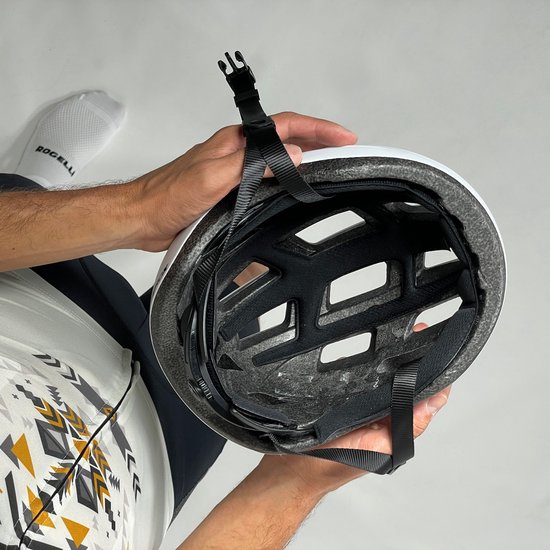 Binnenzijde van een witte Rogelli fietshelm met zwarte bandjes, vastgehouden door handen.
