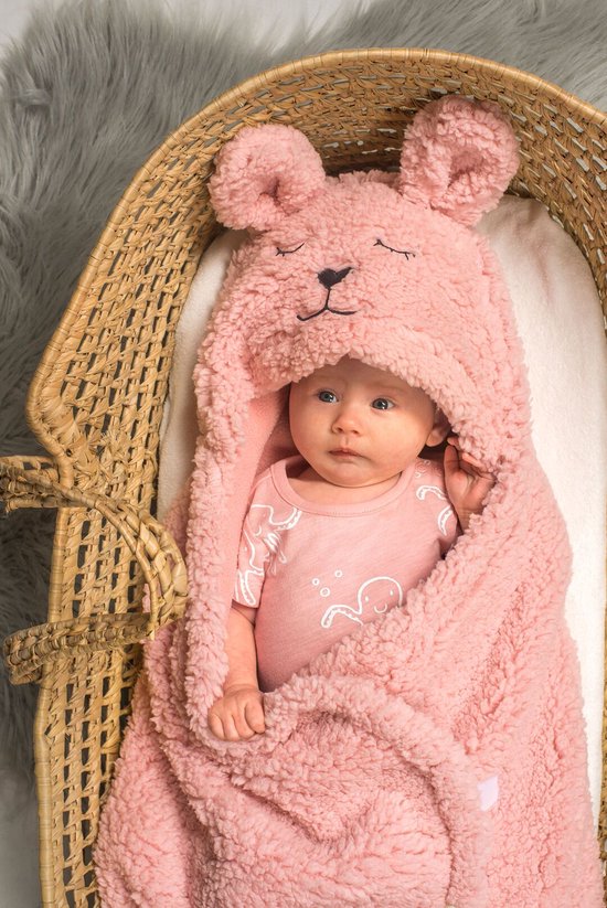 Baby in een roze teddy-wikkeldeken met capuchon met konijnenoren, liggend in een rieten mand.