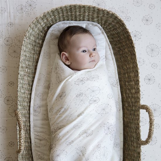Baby, gewikkeld in een lichtgekleurde hydrofiele doek met paardenbloemprint, in een mand.