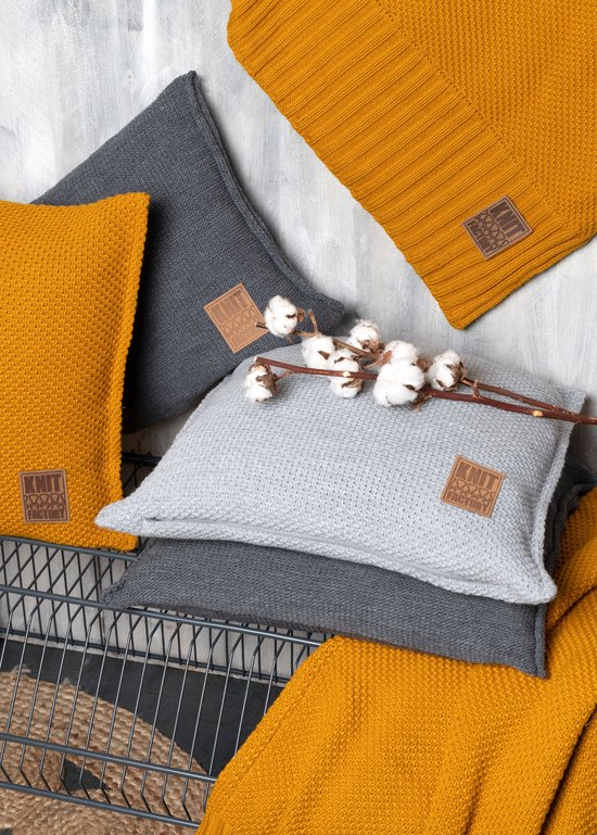 Coussins et plaids tricotés moutarde et gris, avec un coussin gris clair orné de brins de coton.