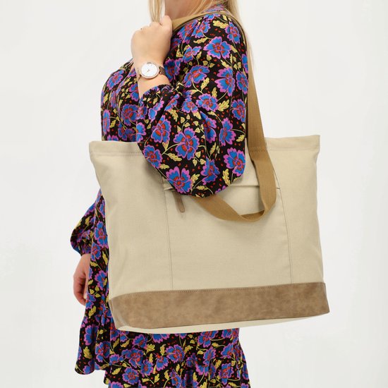 Vrouw met bloemenjurk draagt een lichtbruine canvas shopper tas met bruin suède bodem.