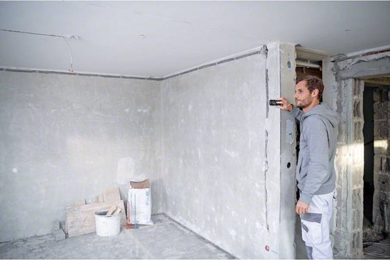 Man in bouw kleding meet een muur met een Bosch laser afstandmeter in een verbouwing.