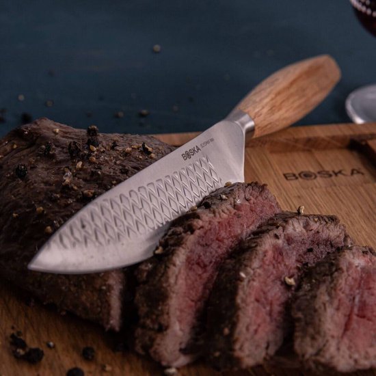 Boska RVS steakmes met houten handvat rust op gesneden rosbief op een houten plank.