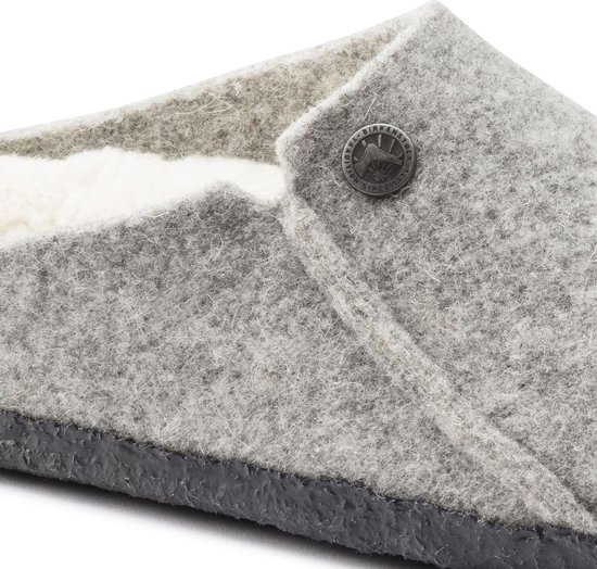 Close-up van een lichtgrijze vilten Birkenstock pantoffel met schapenvacht voering en knoopdetail.