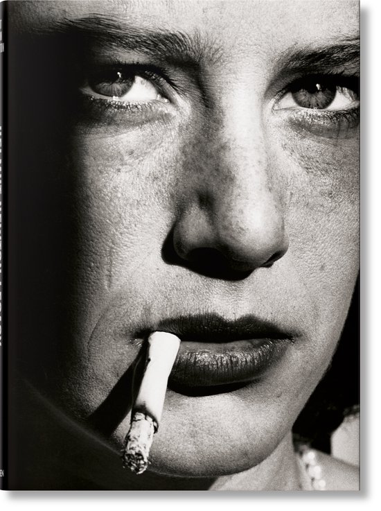Close-up van een vrouw in zwart-wit, rokend met een sigaret tussen haar lippen. "HELMUT NEWTON LEGACY" staat verticaal aan de linkerkant.