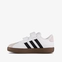 Witte sneaker met zwarte strepen, klittenbandsluiting en bruine zool op witte achtergrond.