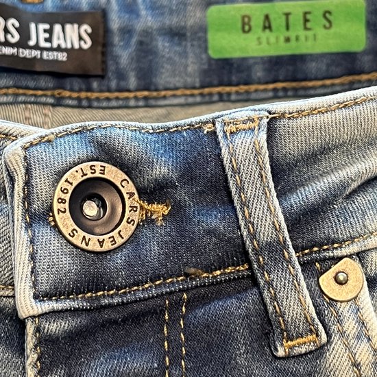 Close-up van de knoopsluiting van de Cars Jeans Bates jeans met 'EST. 1982' erop.