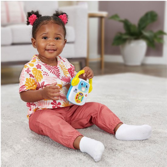 Een jong meisje zit op de grond met een Vtech baby muziekspeler in haar handen.