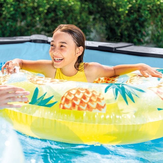 Een lachend meisje in een geel zwempak met een ananas-opblaasband in een zwembad.