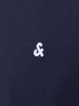 Close-up van het geborduurde witte '&' logo op een donkerblauw T-shirt.