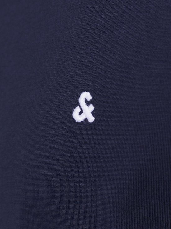 Close-up van het geborduurde witte '&' logo op een donkerblauw T-shirt.