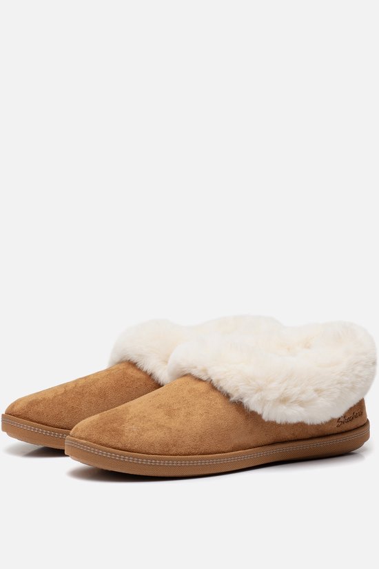 Paar bruine suède pantoffels met dikke, witte nepbontranden. Skechers logo op de zijkant van de rechter pantoffel.