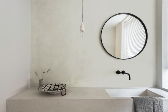 Moderne badkamer met een betonnen wastafel, zwarte kraan en een ronde spiegel.