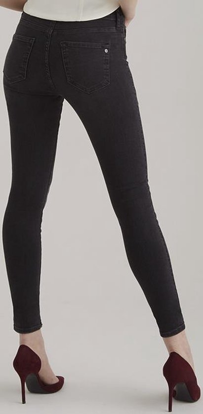 De achterkant van een skinny jeans in de kleur 'black vintage' op een model, met bordeauxrode schoenen.