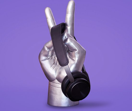 Zilverkleurige hand met twee vingers omhoog, houdt zwarte koptelefoon vast, op paarse achtergrond.