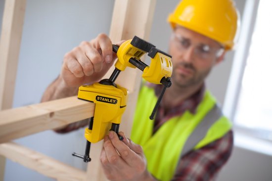 Man met gele helm en veiligheidshesje die een gele multifunctionele boorklem van Stanley gebruikt.