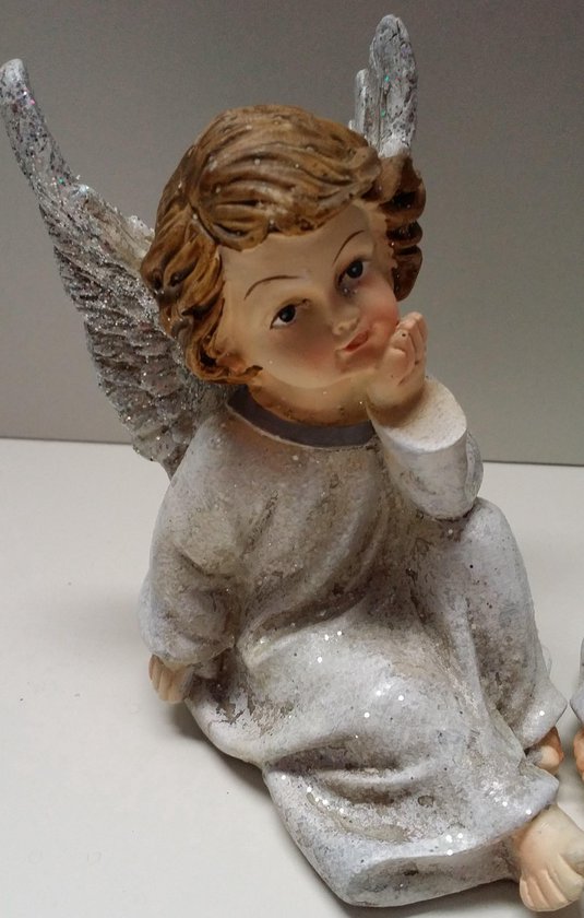 Zittend engeltje in witte jurk met glitter, bruin gekruld haar en denkende pose.