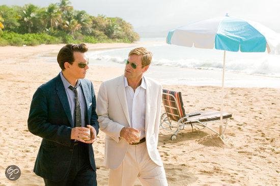 Johnny Depp en Aaron Eckhart lopen op een strand in pakken. Een strandstoel en parasol achter hen.