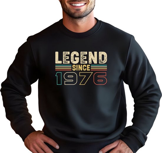 Model draagt een zwarte sweater met vintage opdruk "LEGEND SINCE 1976" in retro kleuren.